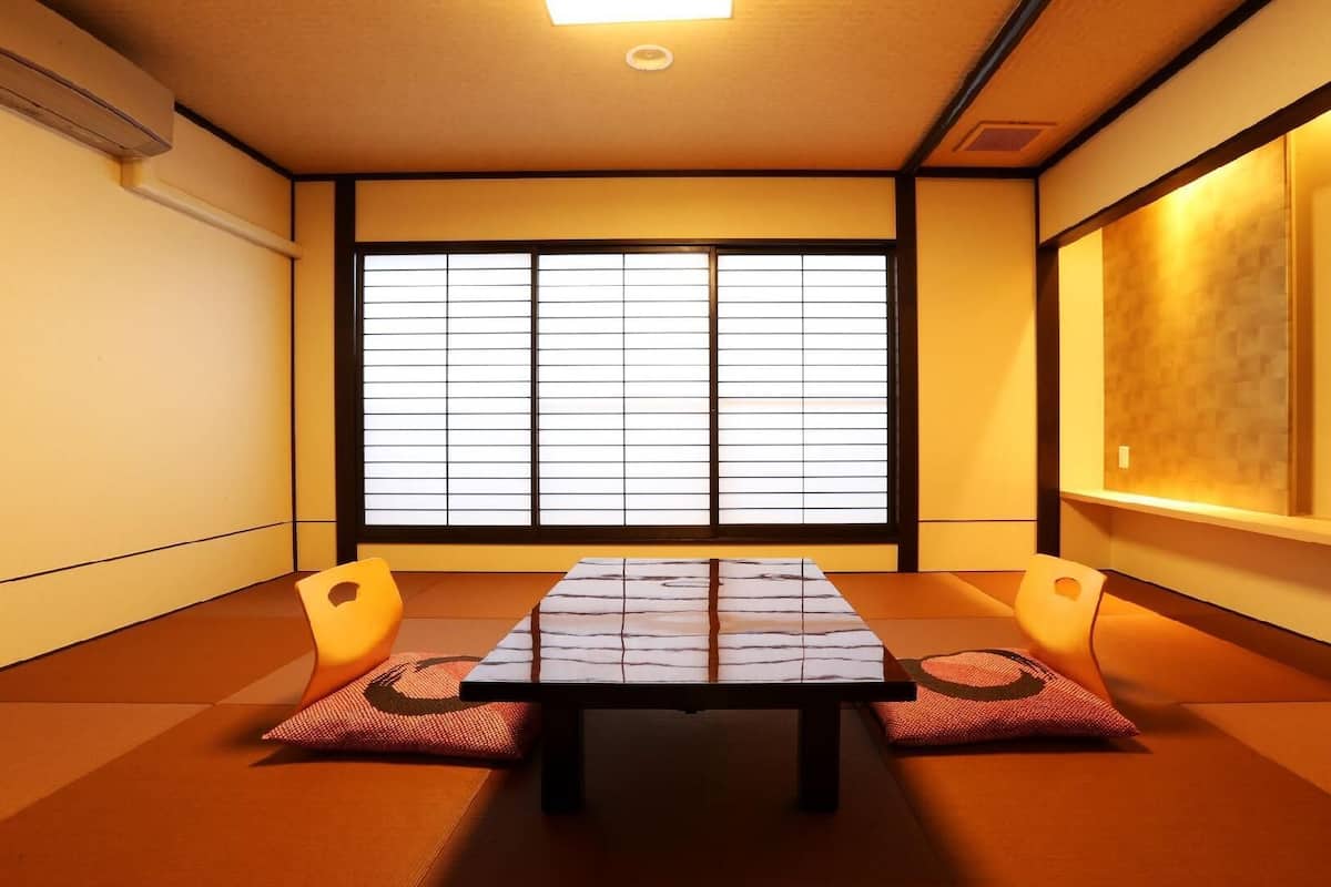 A traditional Japanese room with tatami flooring, a low table, cushions, a sliding shoji screen, and a mounted television.