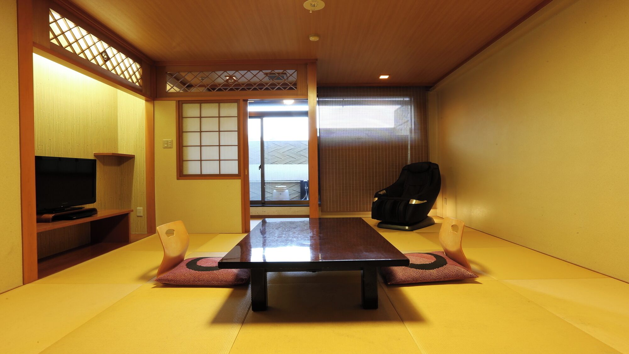 A traditional Japanese room with tatami flooring, a low table, a television, and a massage chair.