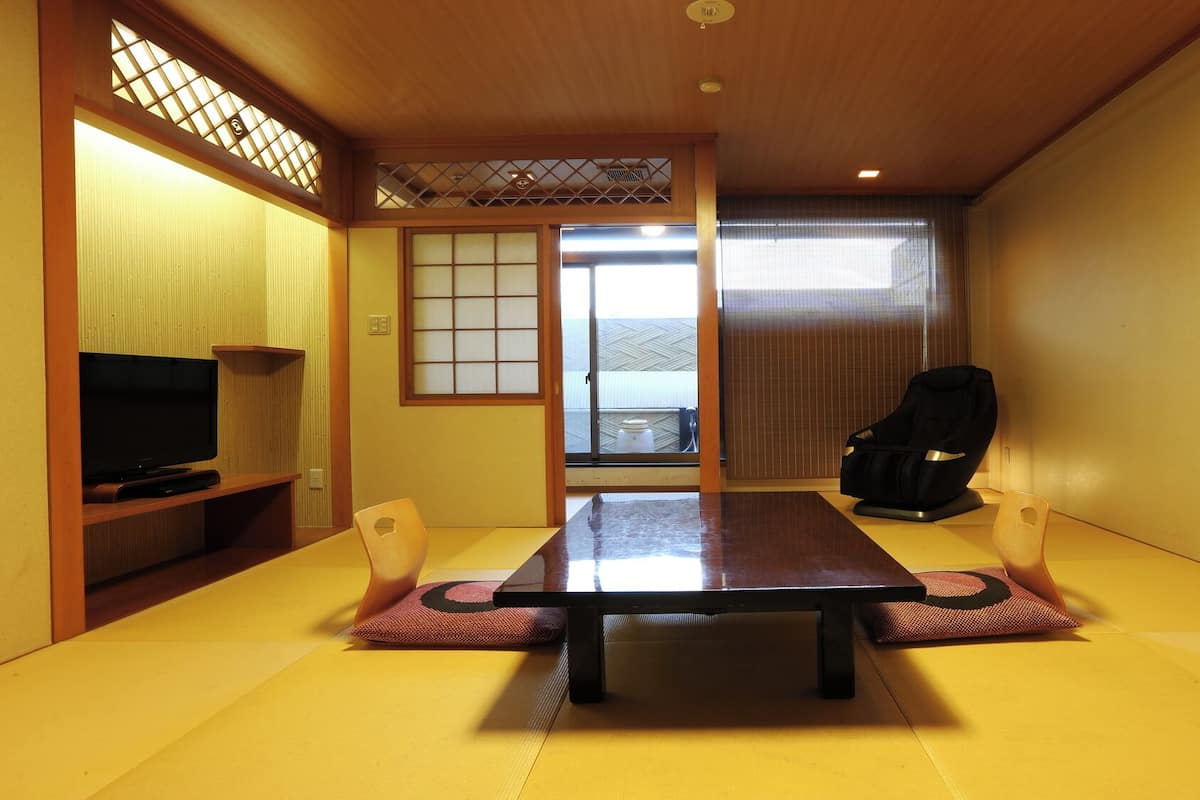 A traditional Japanese room with tatami flooring, a low table, a television, and a massage chair.