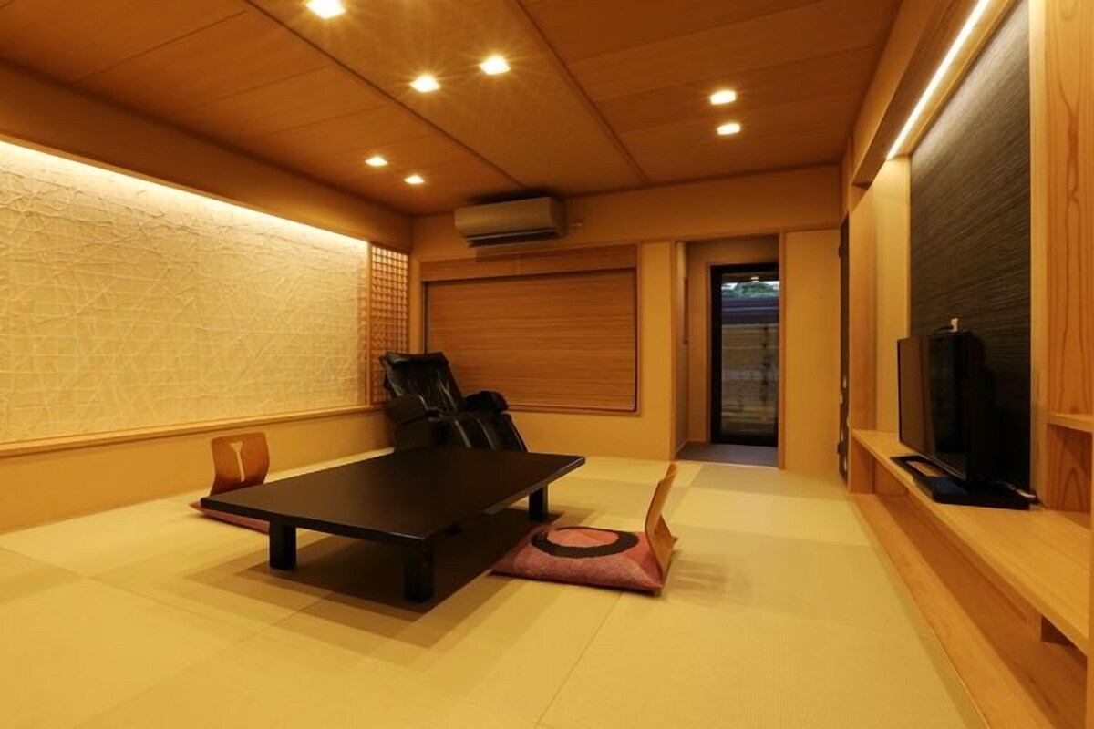 A room with a wooden floor, a black table, a black chair, a television, and a sliding door.