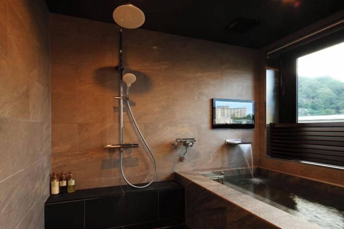 A modern bathroom with a shower, a bathtub, and a window with a view of greenery.