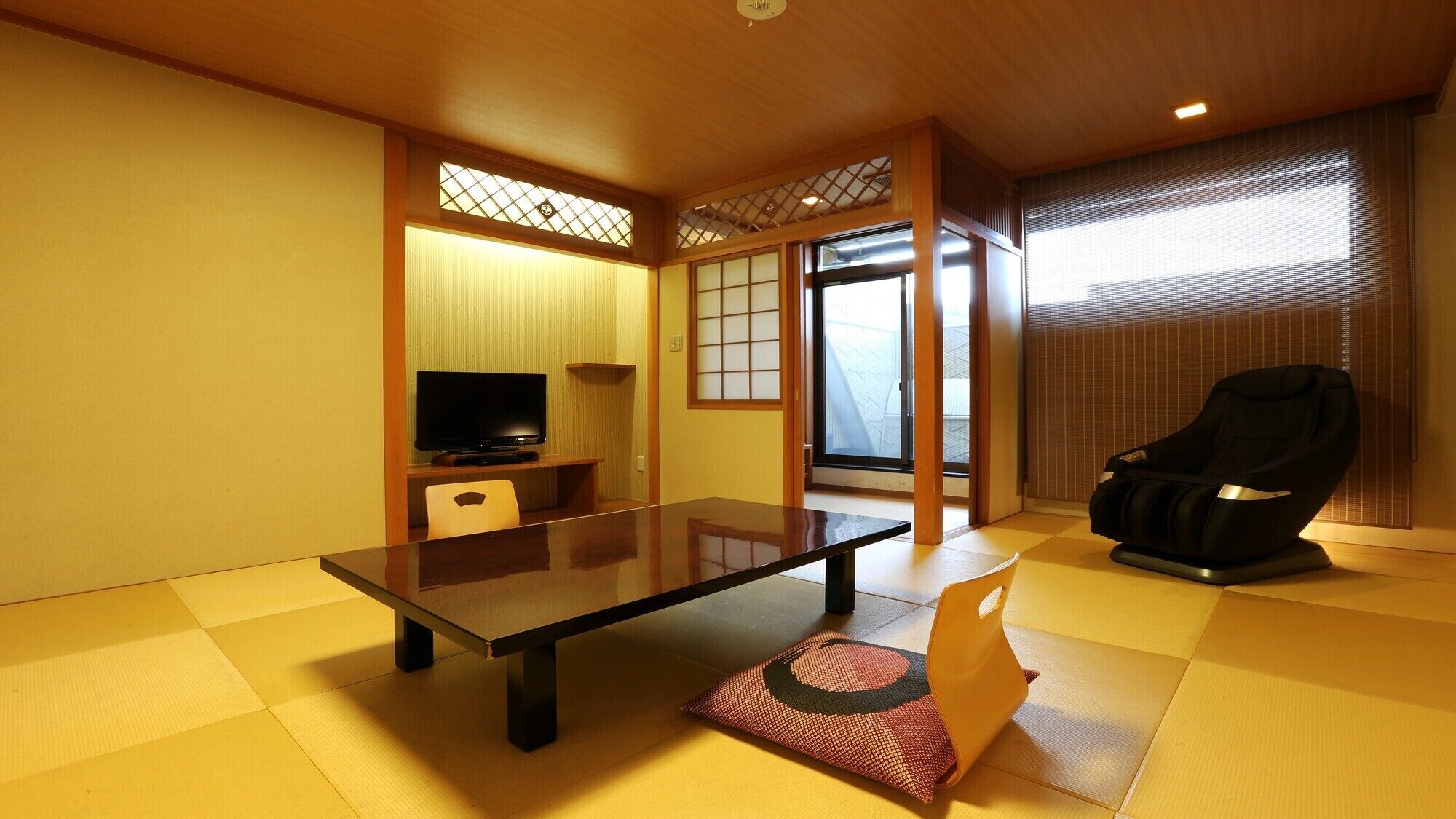 A traditional Japanese-style room with tatami flooring, a low table, a television, a massage chair, and sliding doors.