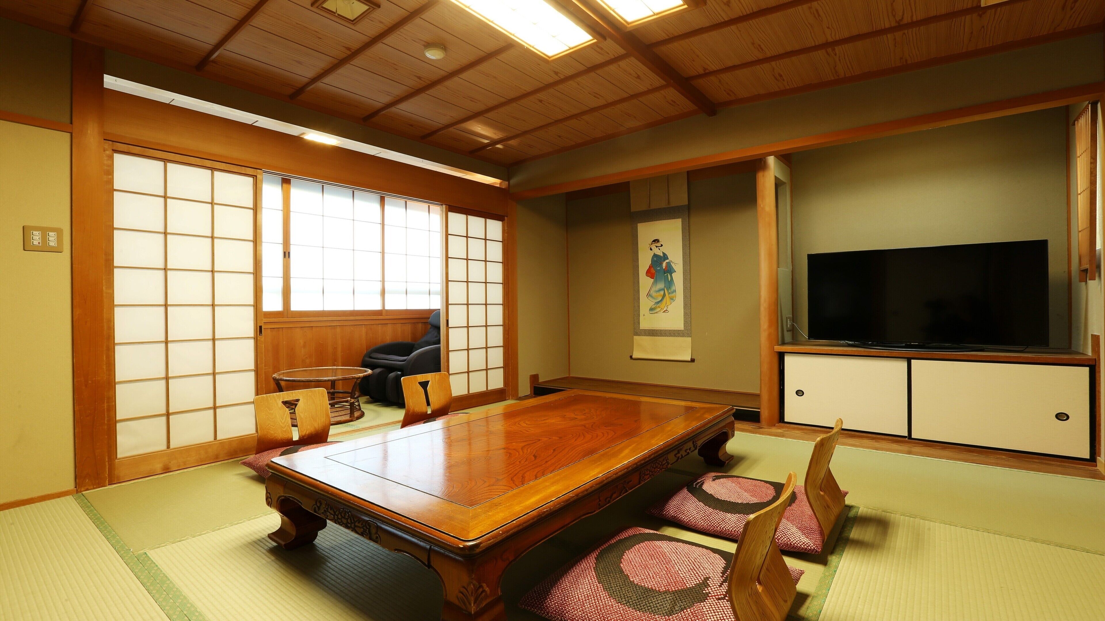 A traditional Japanese room with tatami flooring, a wooden dining table, chairs, a television, and sliding doors.