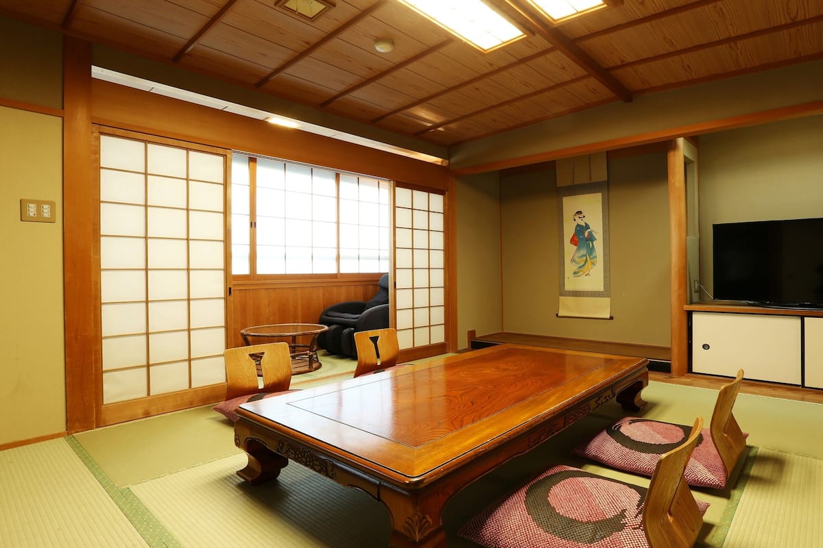 A traditional Japanese room with tatami flooring, a wooden dining table, chairs, a television, and sliding doors.