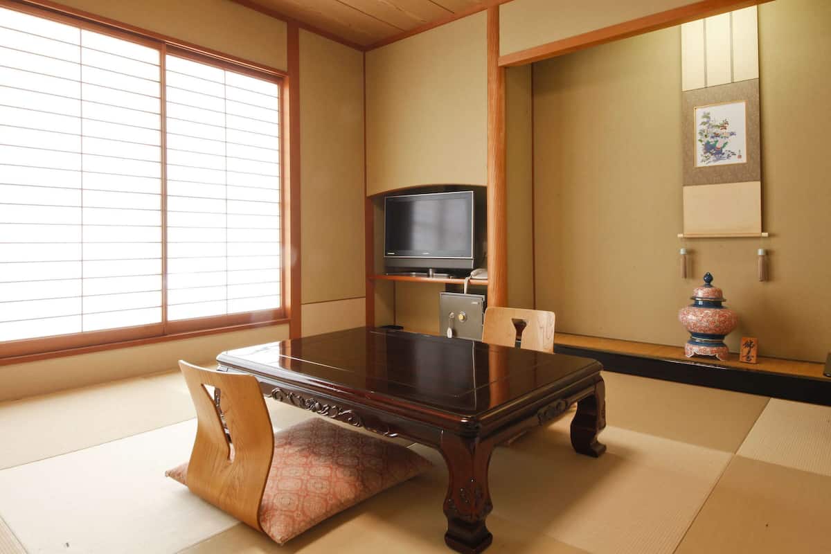 A traditional Japanese room with tatami flooring, a low wooden table, a television, and a decorative vase.