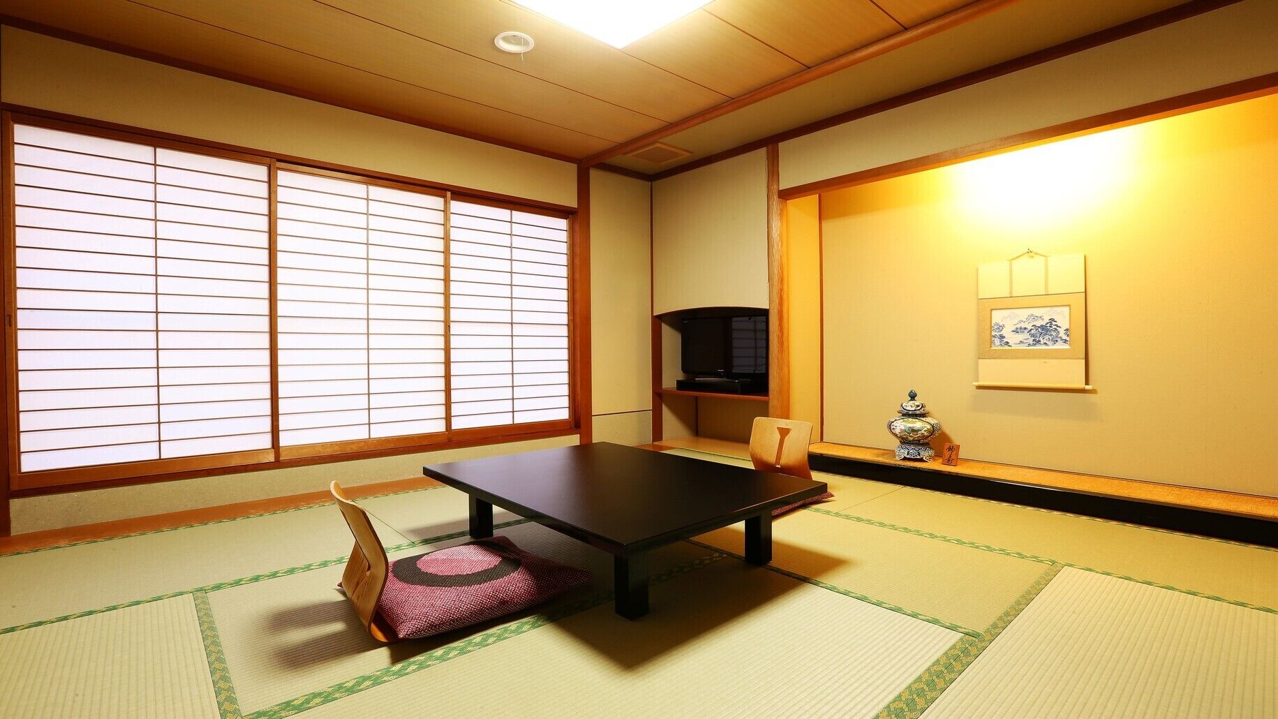 A traditional Japanese room with tatami flooring, a low table, a television, and a decorative vase.