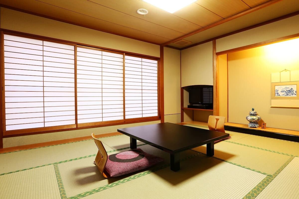 A traditional Japanese room with tatami flooring, a low table, a television, and a decorative vase.