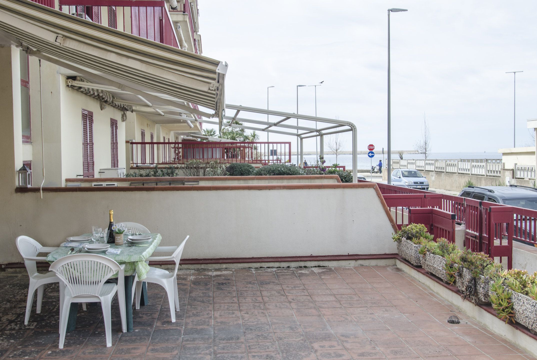 A terrace with a table set for dining, a railing, and a view of the sea.