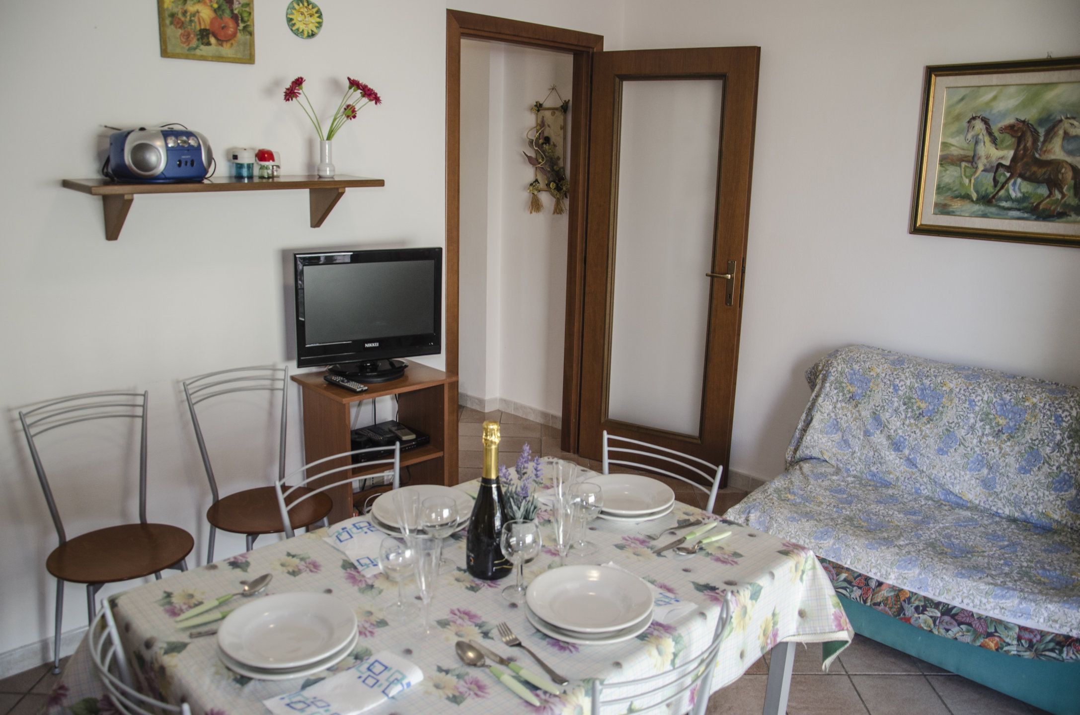 A dining area with a table set for four, a television, and a sofa.