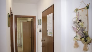 A hallway with a wooden door, a bulletin board, and a decorative wall hanging. - Casa Parago (Alghero)