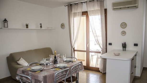 Un coin repas avec une table dressée pour quatre personnes, un canapé et une petite cuisine.