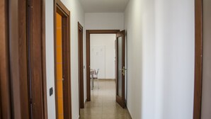 Un couloir avec des portes en bois et un sol carrelé, qui mène à une pièce contenant une chaise et une table.