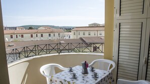 Un balcon avec une table dressée pour quatre personnes, des chaises blanches et une vue sur les bâtiments en arrière-plan.