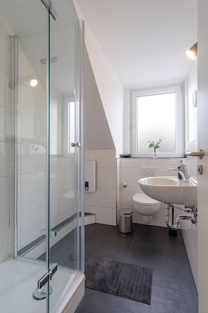 A modern bathroom with a glass shower enclosure, a white sink, and a toilet. - Glück Auf Appartements Am Stadtpark (Duisburg)
