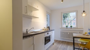 A modern kitchen with white cabinetry, a built-in oven, a sink, and a window with a view of buildings. - Glück Auf Appartements Am Stadtpark (Duisburg)