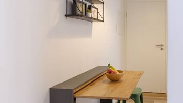Eine moderne Küche mit Holztisch, grünen Hocker, einer Pendelleuchte und einem Wandregal mit Dekorationselementen.