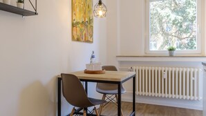 A dining area with a wooden table and chairs, a pendant light, a radiator, and a window with a view of trees. - Glück Auf Appartements Am Stadtpark (Duisburg)