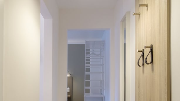 A hallway with a wooden floor, a grey mat, a wooden door with a handle, and a hanging light fixture. - Glück Auf Appartements Am Stadtpark (Duisburg)