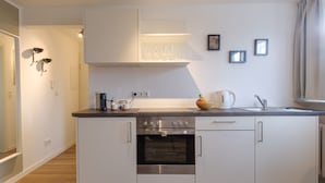 A modern kitchen with white cabinets, a built-in oven, a coffee maker, and a bowl of fruit on the counter. - Glück Auf Appartements Am Stadtpark (Duisburg)