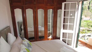 Ein Schlafzimmer mit Bett, Kissen, einem Kleiderschrank und einer Glastür zu einem Außenbereich.