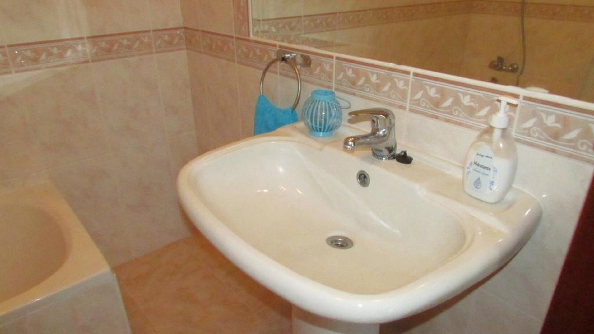 A bathroom with a white sink, a blue towel, and a bottle of hand sanitizer.