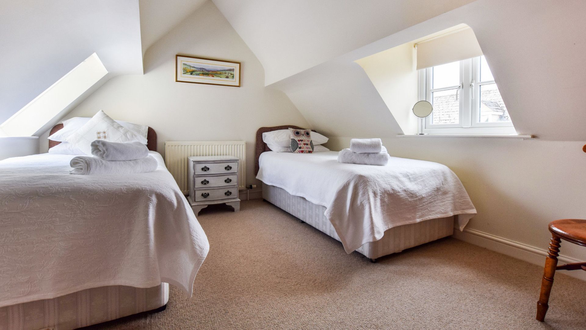 A bedroom with two beds, a nightstand, a radiator, and a window.
