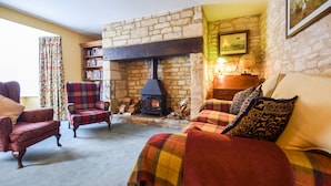 A cozy living room with a stone fireplace, a bookshelf, and a comfortable sofa with plaid throw blankets. - Barebones Farm - sleeps 14 guests  in 7 bedrooms (Winchcombe)