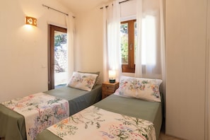 A room with two beds, a nightstand with a lamp, a wall-mounted light, and a window with curtains. - Porto Cervo Villa La Gjanda, surrounded by nature, private heated pool (Arzachena)
