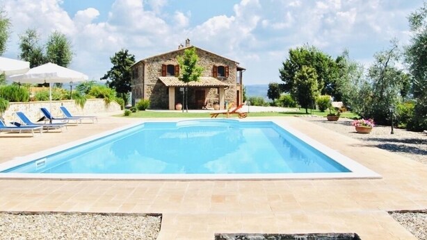 Una casa de piedra con piscina, sillas de descanso y vistas al mar.