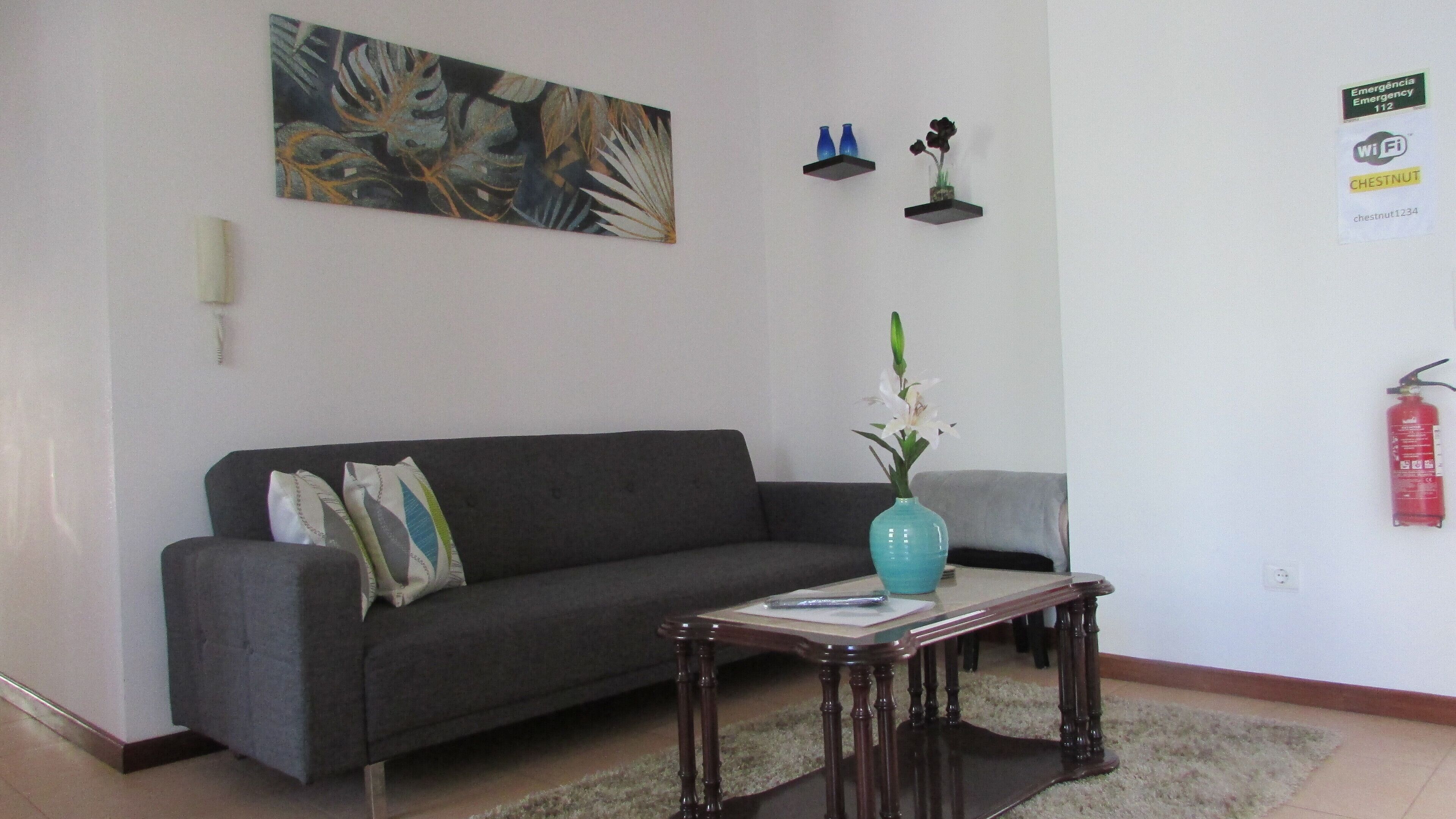 Un salon avec un canapé gris, un vase turquoise orné de fleurs blanches, une petite table et un tableau accroché au mur.
