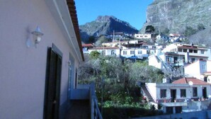 Una cittadina costiera con edifici su una collina, una montagna imponente sullo sfondo e un cielo sereno.