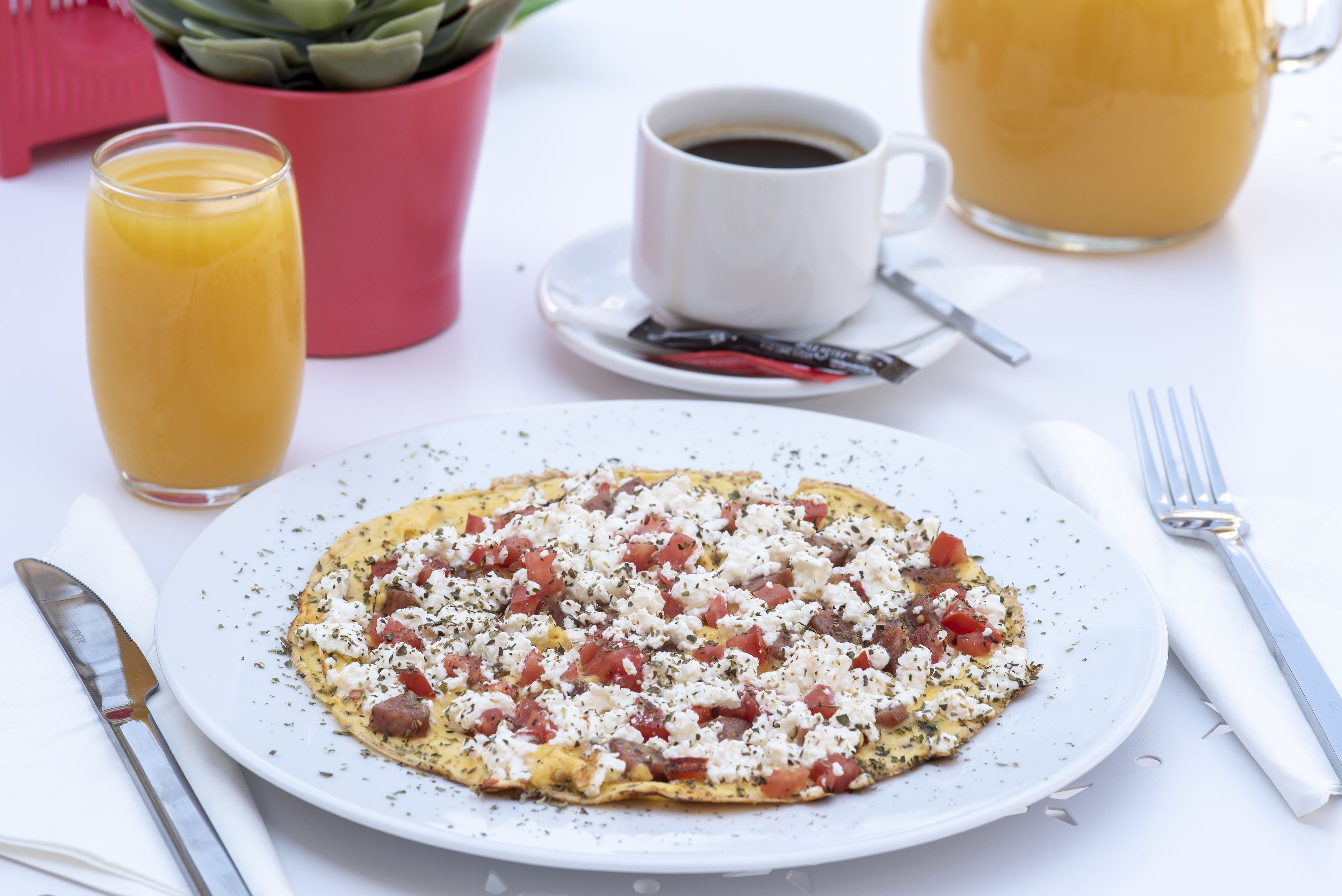 A breakfast setting with a plate of food, a glass of orange juice, a cup of coffee, and a pink container.
