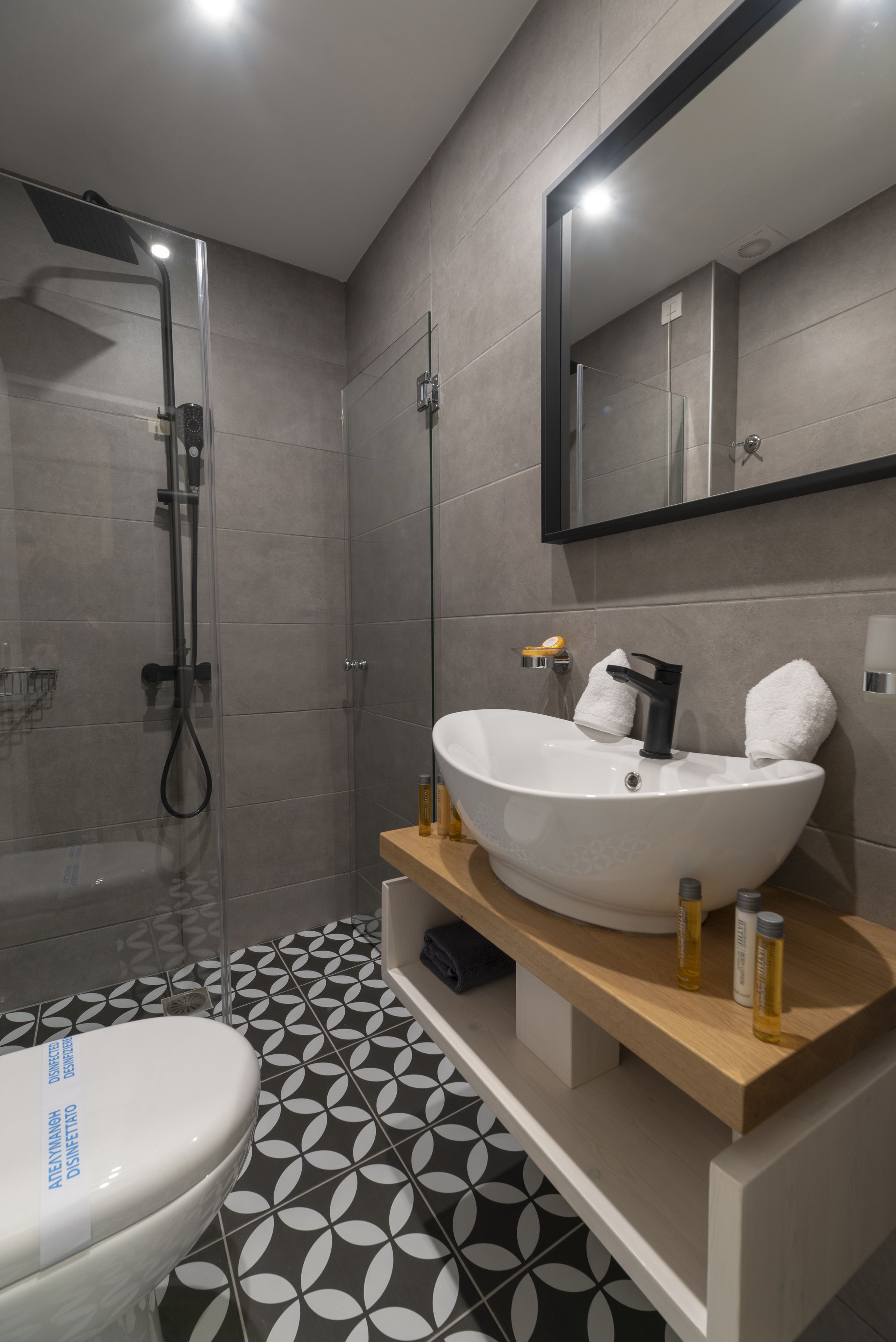 A modern bathroom with a large white sink, a glass shower enclosure, and a patterned floor.
