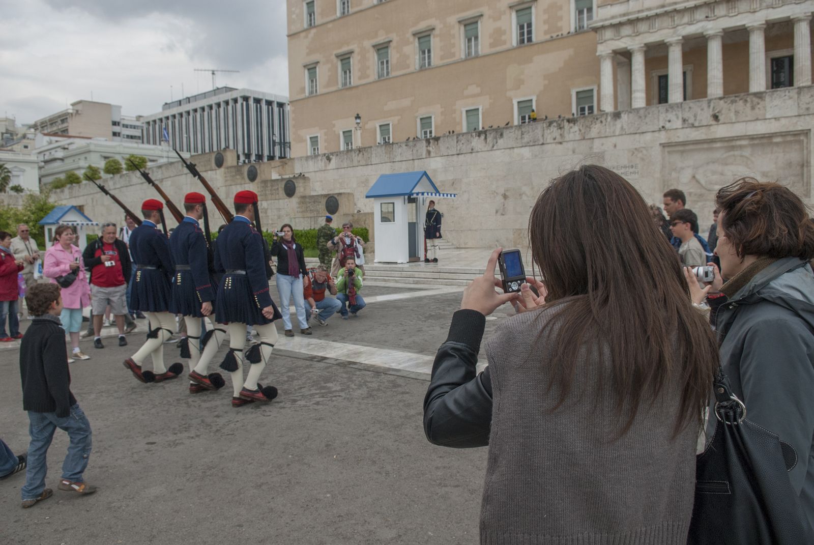A group of uniformed personnel in traditional attire, possibly a ceremonial event, with spectators taking photos.