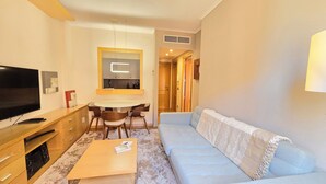 A living room with a TV, sofa, coffee table, and dining area with chairs and a table. - Waterfront Campezo (Madrid)