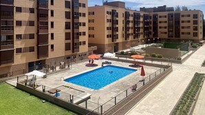 A modern apartment building with a rectangular swimming pool surrounded by a paved deck. - Waterfront Campezo (Madrid)