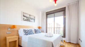 A hotel room with a bed, a nightstand, a lamp, a painting, and a view of the outside. - Waterfront Campezo (Madrid)