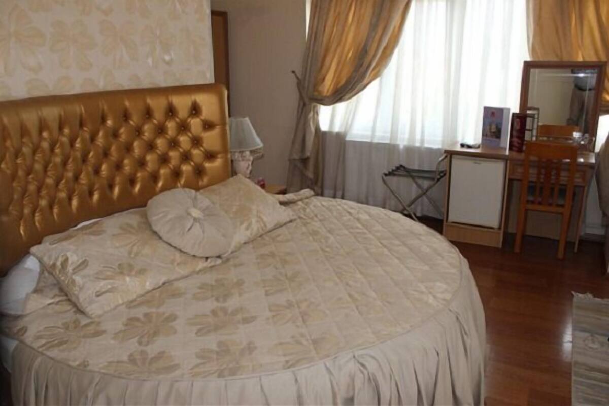 A bedroom with a tufted headboard, a bed with floral bedding, a desk with a chair, and a mirror.