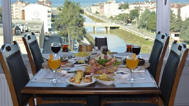 A dining table with a view of a river and buildings, set with plates, glasses, and a variety of food items. - Grand Hotel Tesk (Ordu)