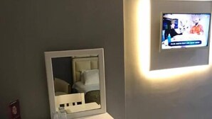 A room with a white desk, a chair, a television mounted on the wall, and a small cabinet. - Grand Hotel Tesk (Ordu)