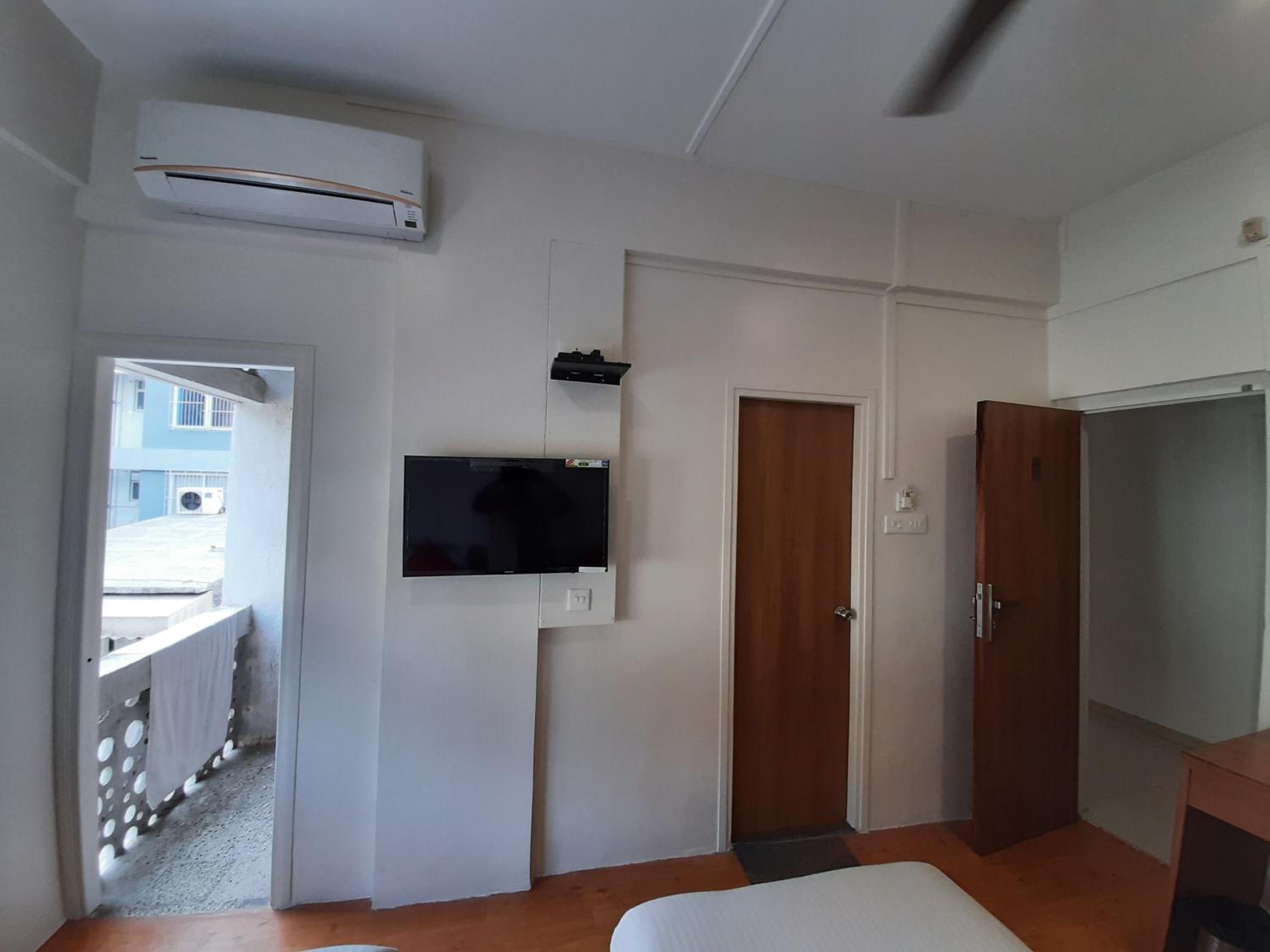 A room with a flat-screen TV mounted on the wall, a wooden wardrobe, and a door.