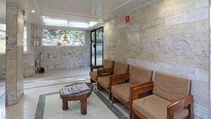 A lobby with marble walls, a stained glass window, and wooden chairs. - Hotel Bhooshan Sivajinagar (Pune)