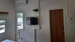 A room with a ceiling fan, an air conditioning unit, a television mounted on the wall, and a wooden door. - Hotel Bhooshan Sivajinagar (Pune)