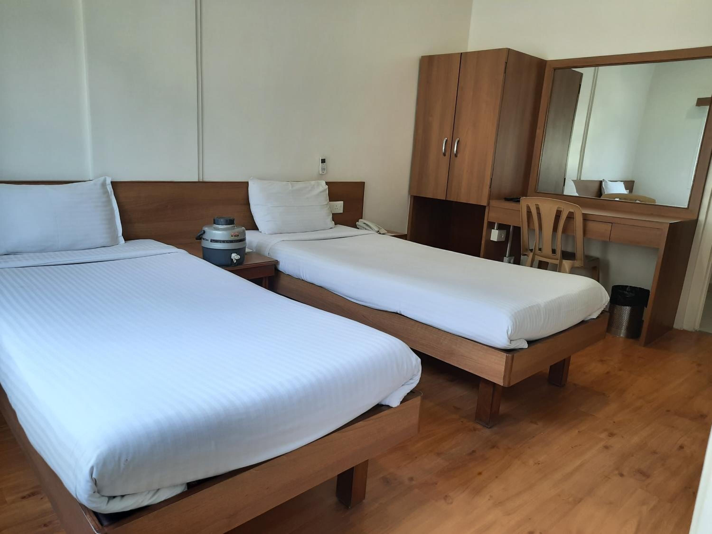 Habitación de hotel con dos camas individuales, un escritorio de madera con espejo y una kitchenette pequeña.