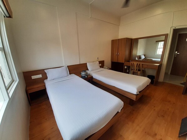 A room with two single beds, wooden furniture, a desk, and a mirror.