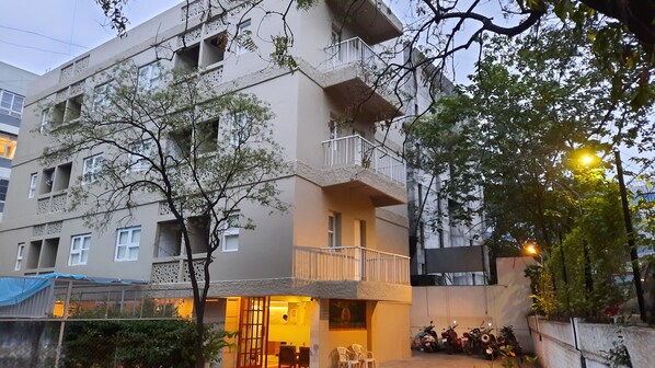 Un immeuble à plusieurs étages doté de balcons, d’une entrée sécurisée et d’une rangée de scooters garés.