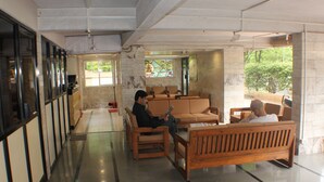 A spacious lobby with a wooden bench seating area, a reception desk, and a large window with a view of greenery outside. - Hotel Bhooshan Sivajinagar (Pune)