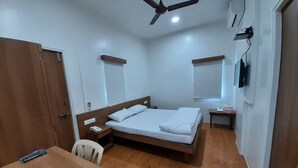 A bedroom with a wooden bed, a desk, a chair, a ceiling fan, and a TV mounted on the wall. - Hotel Bhooshan Sivajinagar (Pune)