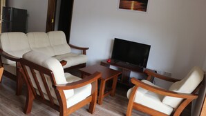 Una sala de estar con un sofá, dos sillones de madera, una mesa de centro y un televisor de pantalla plana.
