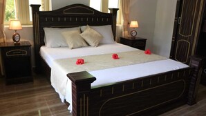 Una cama bien hecha con un cabecero de madera, dos mesitas de noche con lámparas, y un armario de madera oscura.
